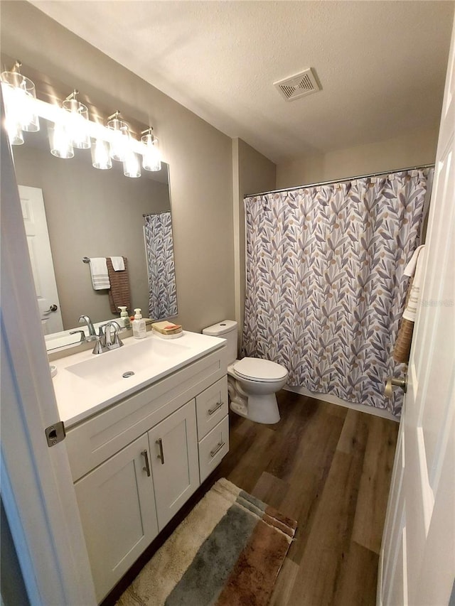 bathroom with curtained shower, a textured ceiling, hardwood / wood-style floors, toilet, and vanity