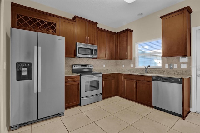 kitchen featuring tasteful backsplash, light tile patterned floors, appliances with stainless steel finishes, light stone countertops, and sink