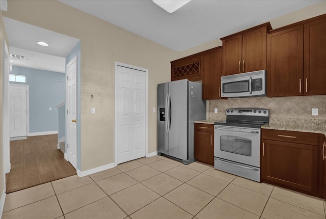 kitchen featuring stainless steel appliances, light stone countertops, light tile patterned floors, and tasteful backsplash