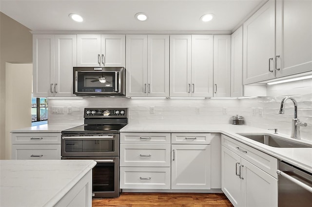 kitchen featuring sink, decorative backsplash, appliances with stainless steel finishes, white cabinetry, and wood-type flooring