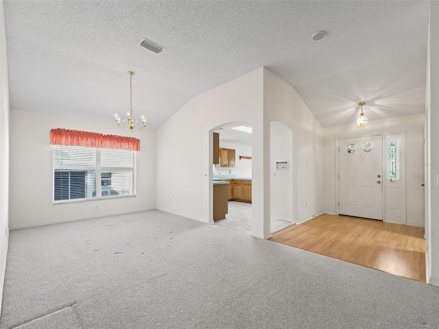 unfurnished living room featuring light carpet, a notable chandelier, and vaulted ceiling