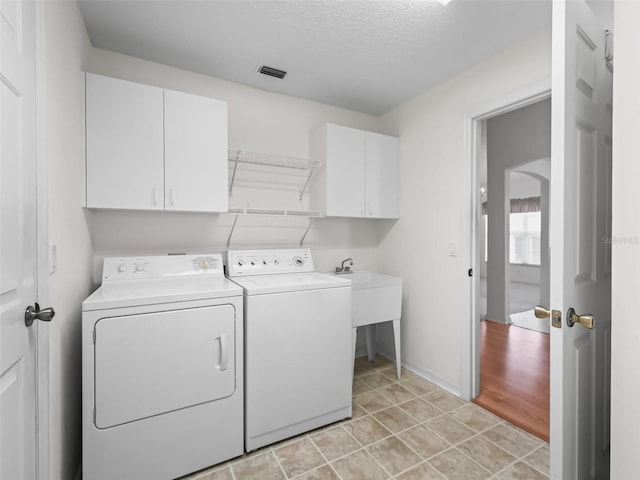 washroom featuring washing machine and dryer, a textured ceiling, light hardwood / wood-style floors, and cabinets