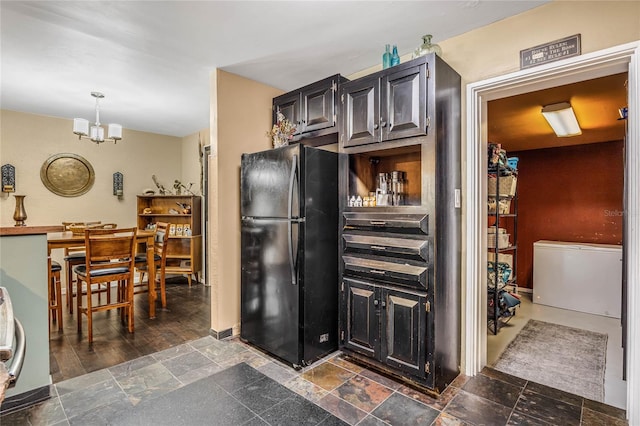 kitchen with dark wood-type flooring, pendant lighting, a chandelier, and black fridge