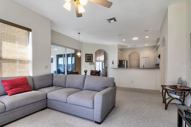 carpeted living room with a textured ceiling and ceiling fan with notable chandelier