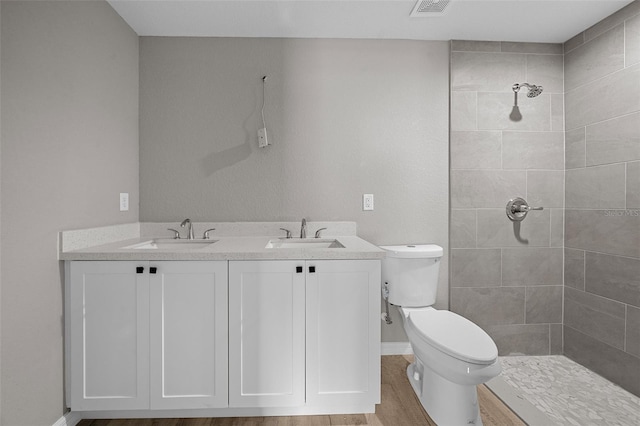 bathroom with toilet, vanity, wood-type flooring, and a tile shower