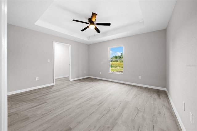 empty room featuring light hardwood / wood-style floors, a tray ceiling, and ceiling fan