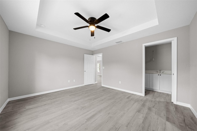 unfurnished bedroom with light hardwood / wood-style floors, a tray ceiling, and ceiling fan