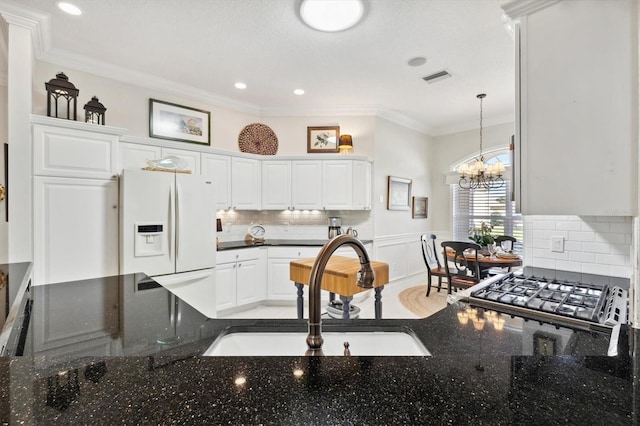 kitchen featuring white fridge with ice dispenser, sink, white cabinets, ornamental molding, and an inviting chandelier