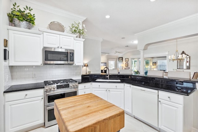 kitchen with kitchen peninsula, stainless steel appliances, sink, decorative columns, and white cabinets