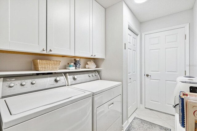 clothes washing area with cabinets, light tile patterned flooring, and washer and clothes dryer