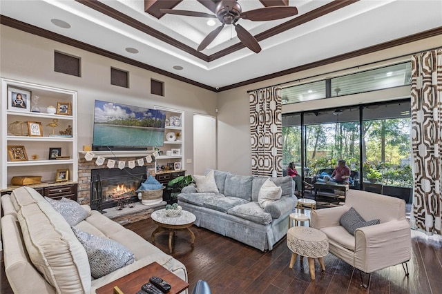 living room with built in features, a fireplace, ceiling fan, crown molding, and dark wood-type flooring