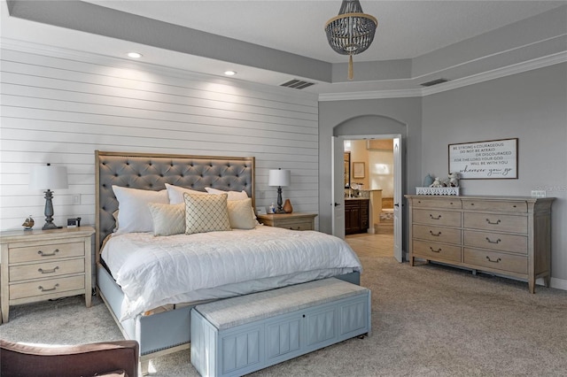 carpeted bedroom with a tray ceiling, connected bathroom, crown molding, and wood walls