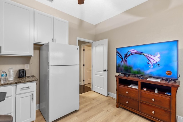 kitchen with dark stone countertops, white cabinets, white refrigerator, ceiling fan, and light hardwood / wood-style flooring