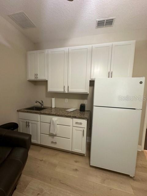 kitchen with sink, light hardwood / wood-style floors, white cabinets, and white refrigerator