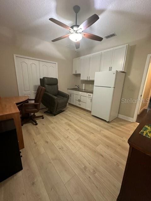 kitchen with ceiling fan, white fridge, white cabinets, and light wood-type flooring