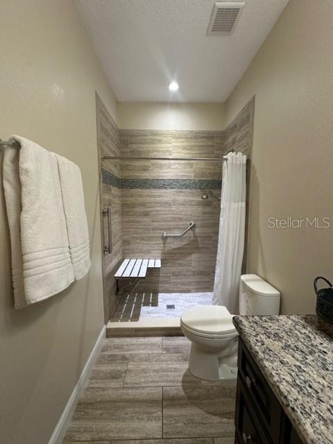 bathroom with vanity, curtained shower, a textured ceiling, and toilet