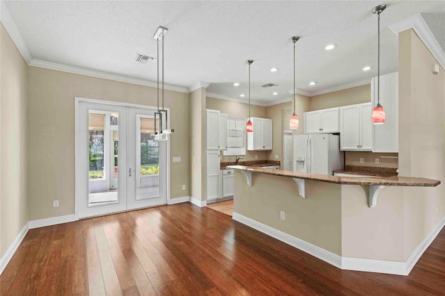 kitchen featuring white cabinetry, white refrigerator with ice dispenser, dark stone counters, kitchen peninsula, and a breakfast bar