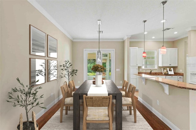 dining area with a textured ceiling, crown molding, wood-type flooring, and sink