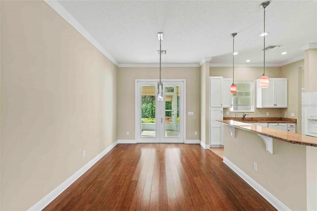 kitchen with white cabinetry, decorative light fixtures, light stone countertops, crown molding, and a breakfast bar