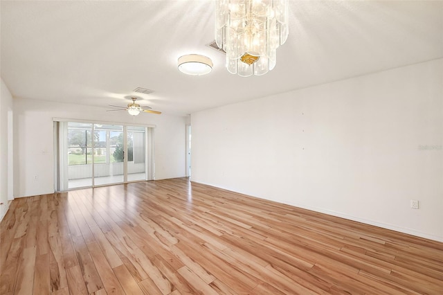 empty room with ceiling fan with notable chandelier and light wood-type flooring