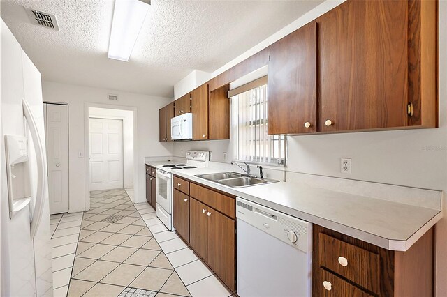 kitchen featuring a textured ceiling, sink, light tile patterned floors, and white appliances