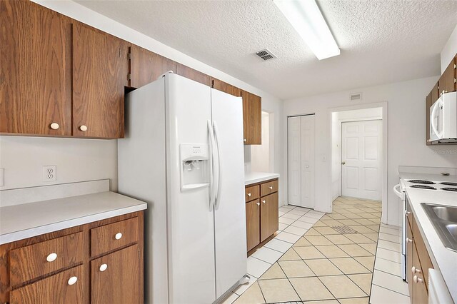 kitchen featuring white appliances, a textured ceiling, and light tile patterned floors