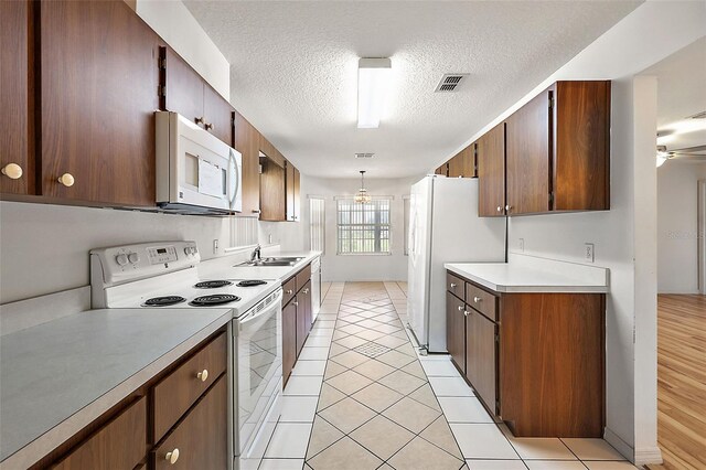 kitchen with white appliances, sink, a textured ceiling, hanging light fixtures, and light tile patterned floors