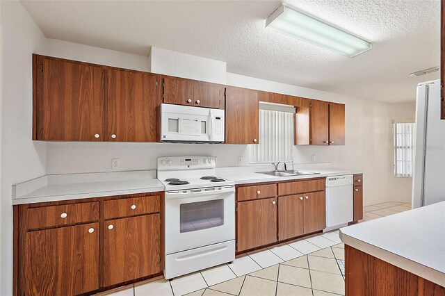 kitchen with light tile patterned flooring, a textured ceiling, sink, and white appliances