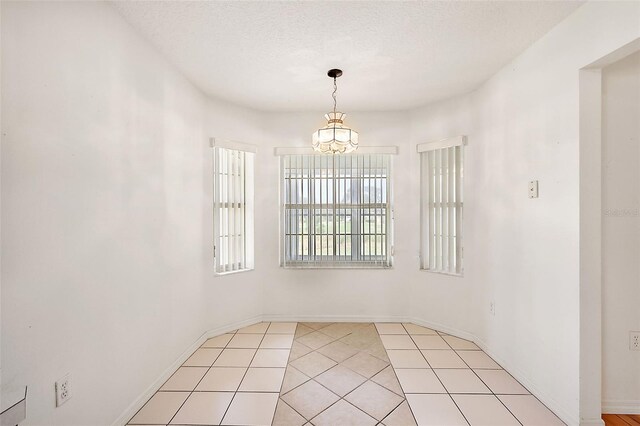 spare room with light tile patterned flooring, a textured ceiling, and an inviting chandelier