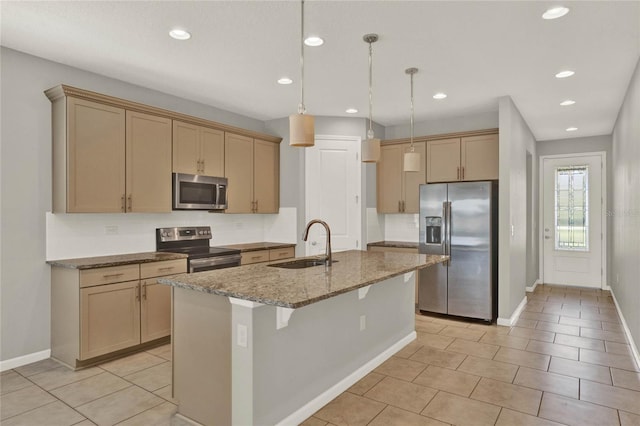 kitchen featuring an island with sink, hanging light fixtures, sink, appliances with stainless steel finishes, and light stone counters