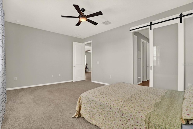 carpeted bedroom with a barn door and ceiling fan