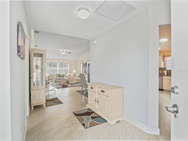 hallway with a textured ceiling, light tile patterned flooring, and vaulted ceiling