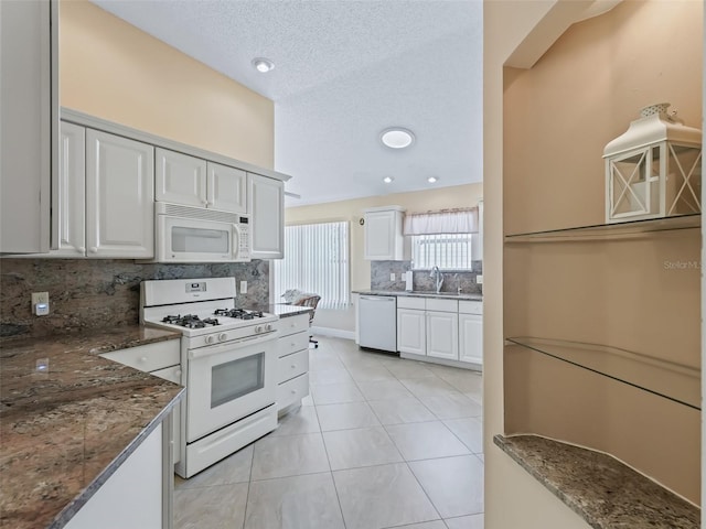 kitchen featuring white cabinetry, dark stone countertops, sink, and white appliances