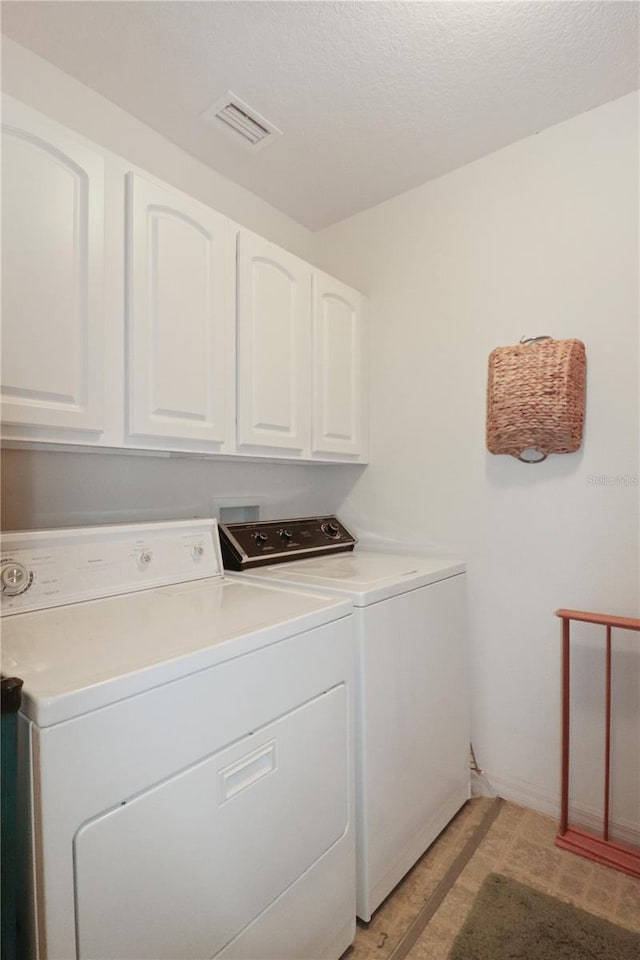 washroom with a textured ceiling, washing machine and clothes dryer, and cabinets