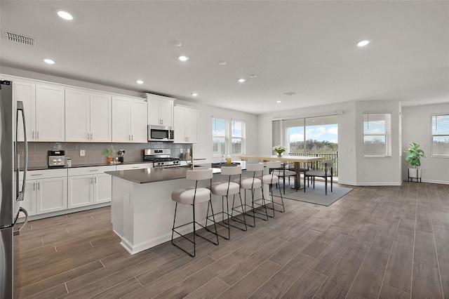 kitchen featuring white cabinetry, stainless steel appliances, wood-type flooring, and an island with sink