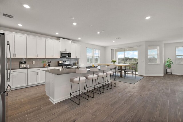 1180 Dora Parc Ln, Mount Dora, FL 32757 - kitchen featuring stainless steel appliances, dark wood-style flooring, an island with sink, backsplash, and white cabinetry
