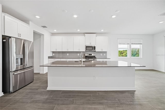 kitchen with dark hardwood / wood-style floors, appliances with stainless steel finishes, a kitchen island with sink, and white cabinetry