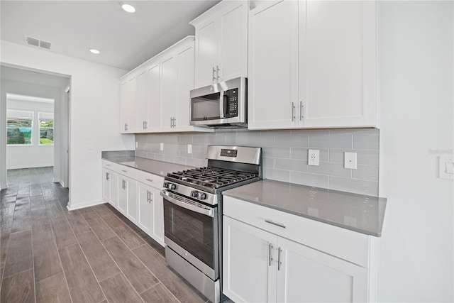 kitchen with backsplash, appliances with stainless steel finishes, white cabinets, and light hardwood / wood-style floors