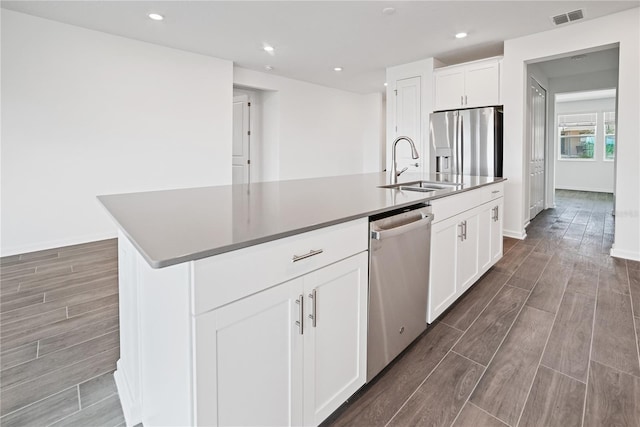 kitchen with appliances with stainless steel finishes, white cabinetry, sink, and a center island with sink