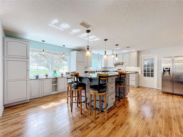 kitchen featuring light wood-type flooring, a kitchen island, a kitchen breakfast bar, white cabinetry, and stainless steel fridge