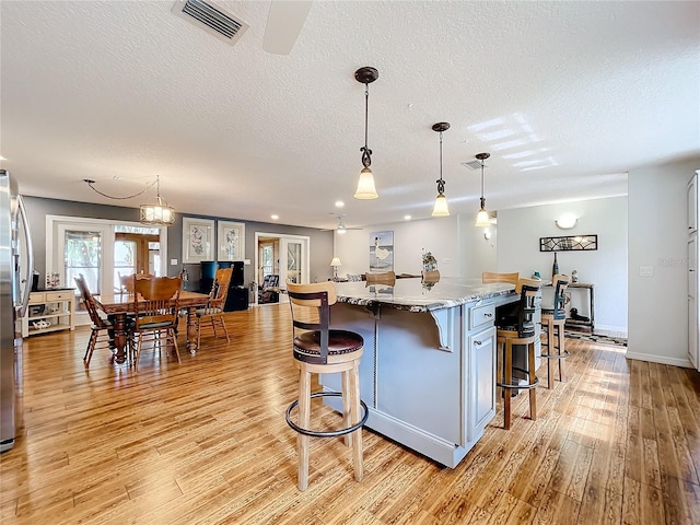 kitchen with a kitchen island, a textured ceiling, light hardwood / wood-style flooring, pendant lighting, and light stone counters