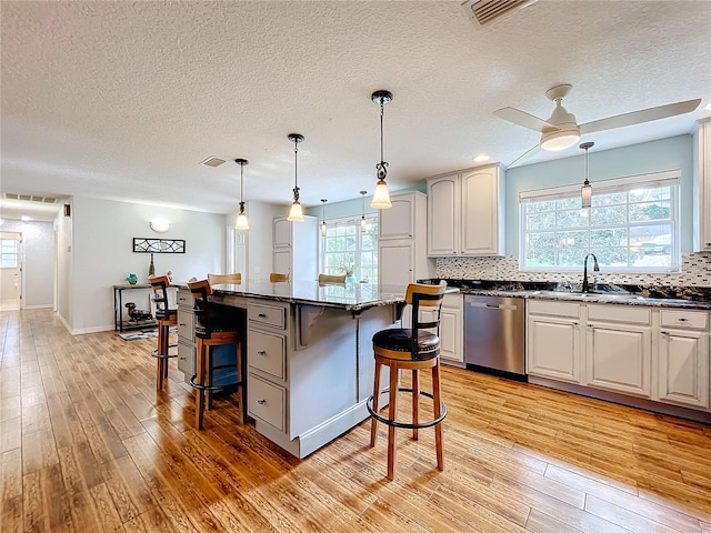 kitchen featuring a center island, light hardwood / wood-style floors, stainless steel dishwasher, dark stone countertops, and a breakfast bar