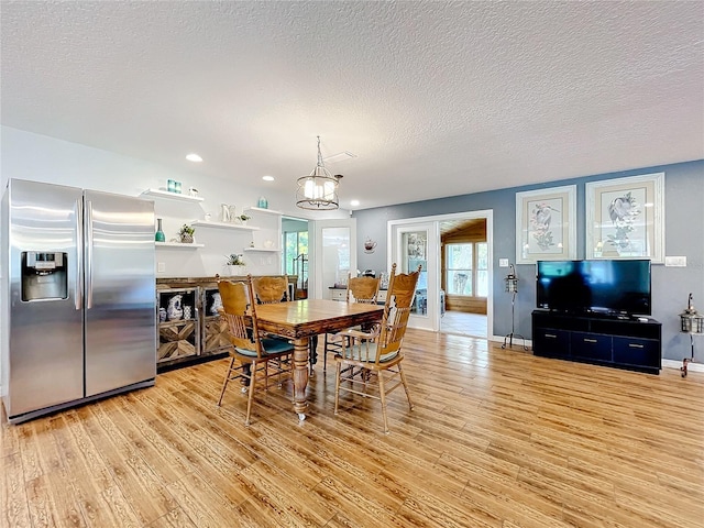 dining area with light hardwood / wood-style floors, an inviting chandelier, and a textured ceiling