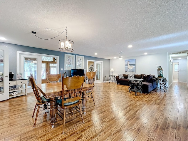 dining space with light hardwood / wood-style floors, a textured ceiling, and ceiling fan with notable chandelier