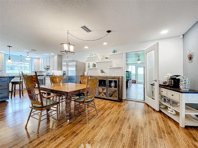 dining room featuring ceiling fan with notable chandelier, a textured ceiling, and light wood-type flooring