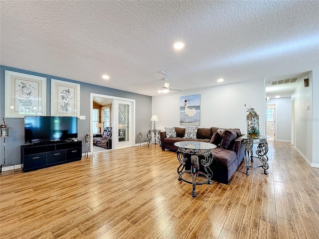 living room with light hardwood / wood-style flooring, a textured ceiling, and ceiling fan