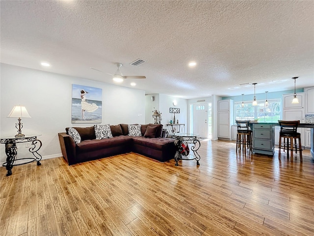 living room with light hardwood / wood-style floors, a textured ceiling, and ceiling fan