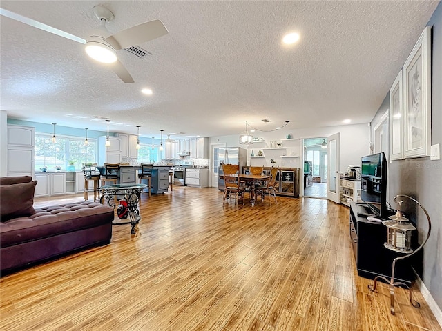 living room with light hardwood / wood-style flooring, a textured ceiling, and ceiling fan