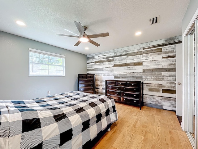 bedroom featuring light hardwood / wood-style floors, a textured ceiling, wooden walls, and ceiling fan