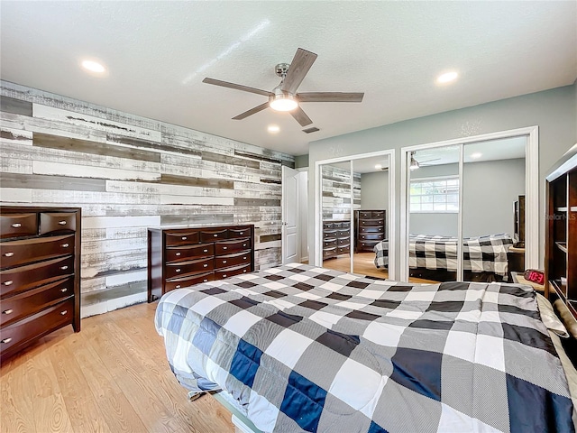 bedroom with ceiling fan, light wood-type flooring, wooden walls, and two closets